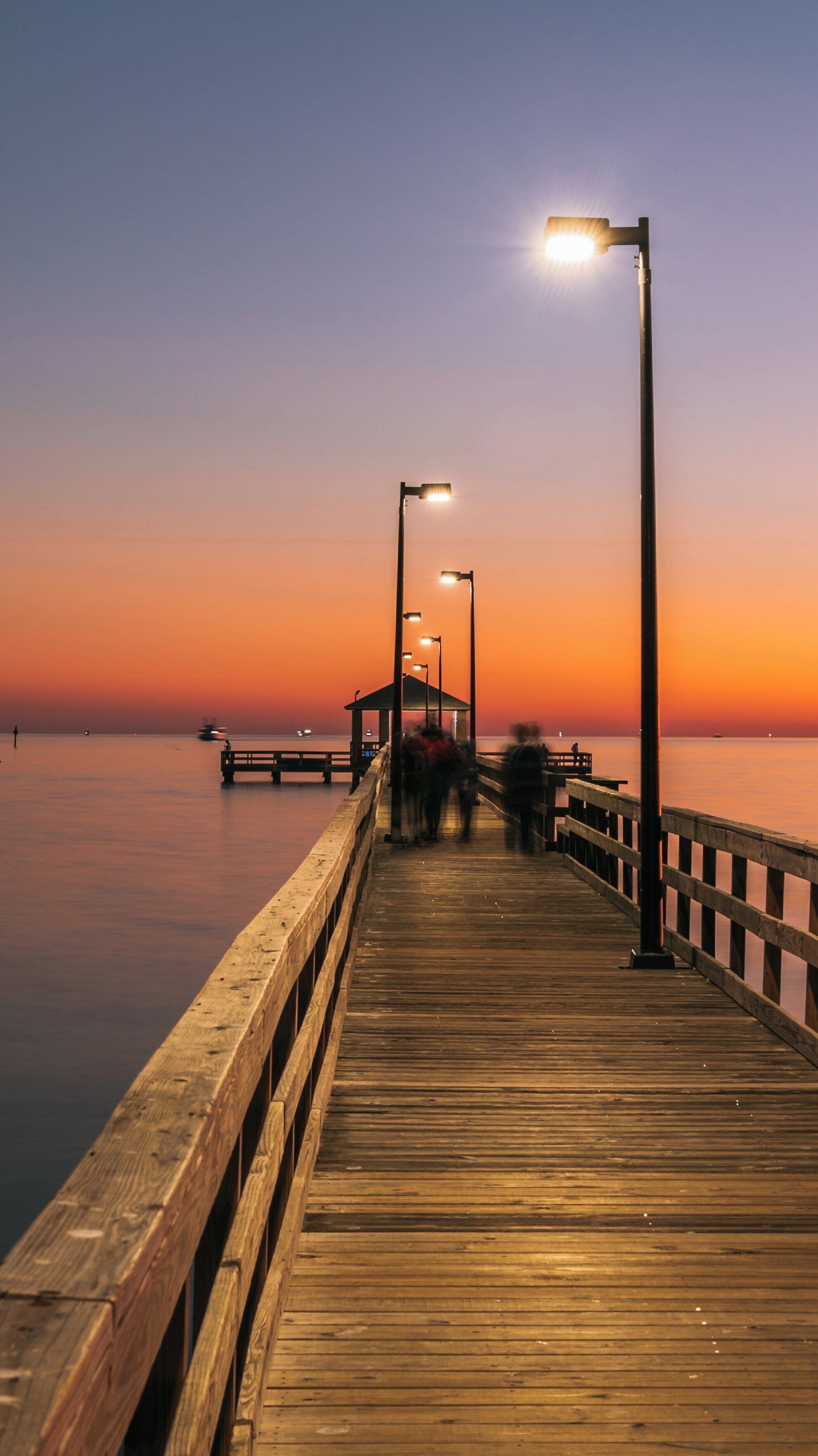 Beautiful sunset over Biloxi Beach with people walking along the wooden pier, capturing the serene atmosphere of Mississippi