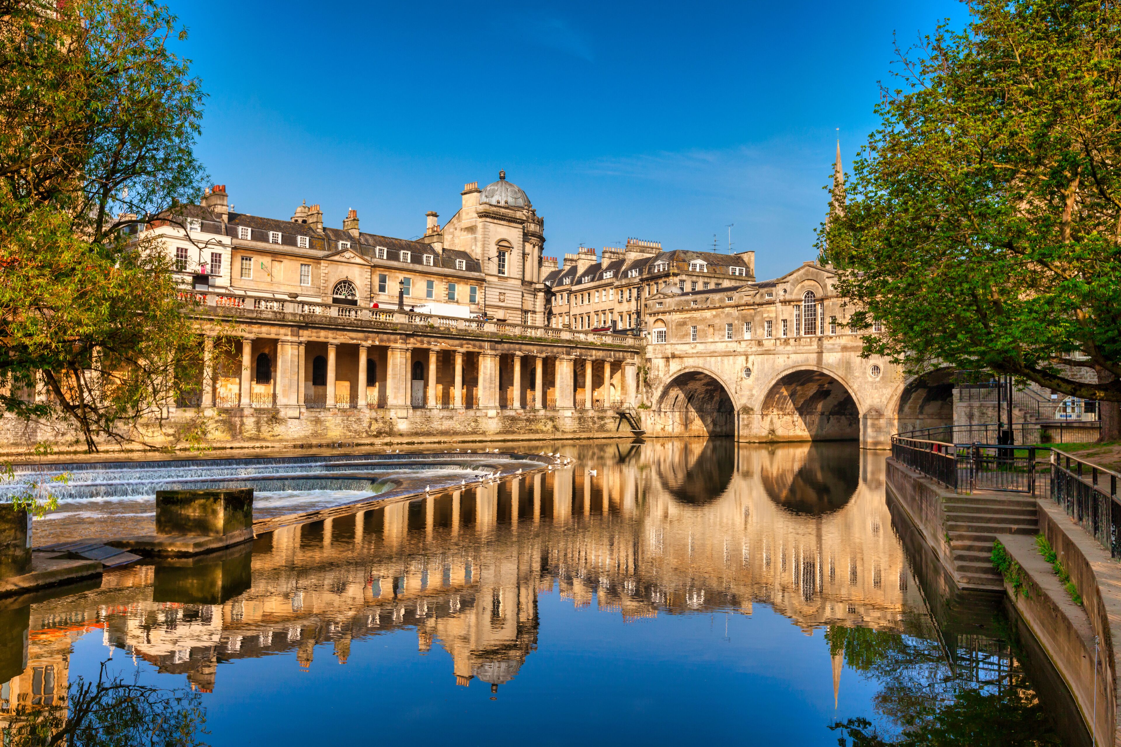 Un bâtiment historique, avec des ponts en arc de cercle enjambant une rivière paisible, dont l’architecture se reflète dans l’eau.