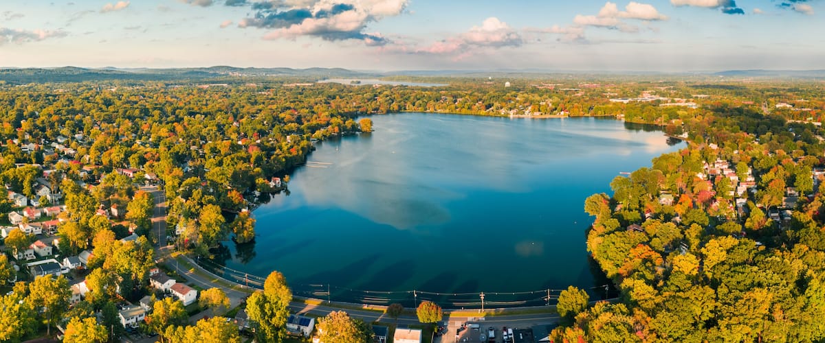 A lake surrounded by a densely wooded area with houses and a clear sky.