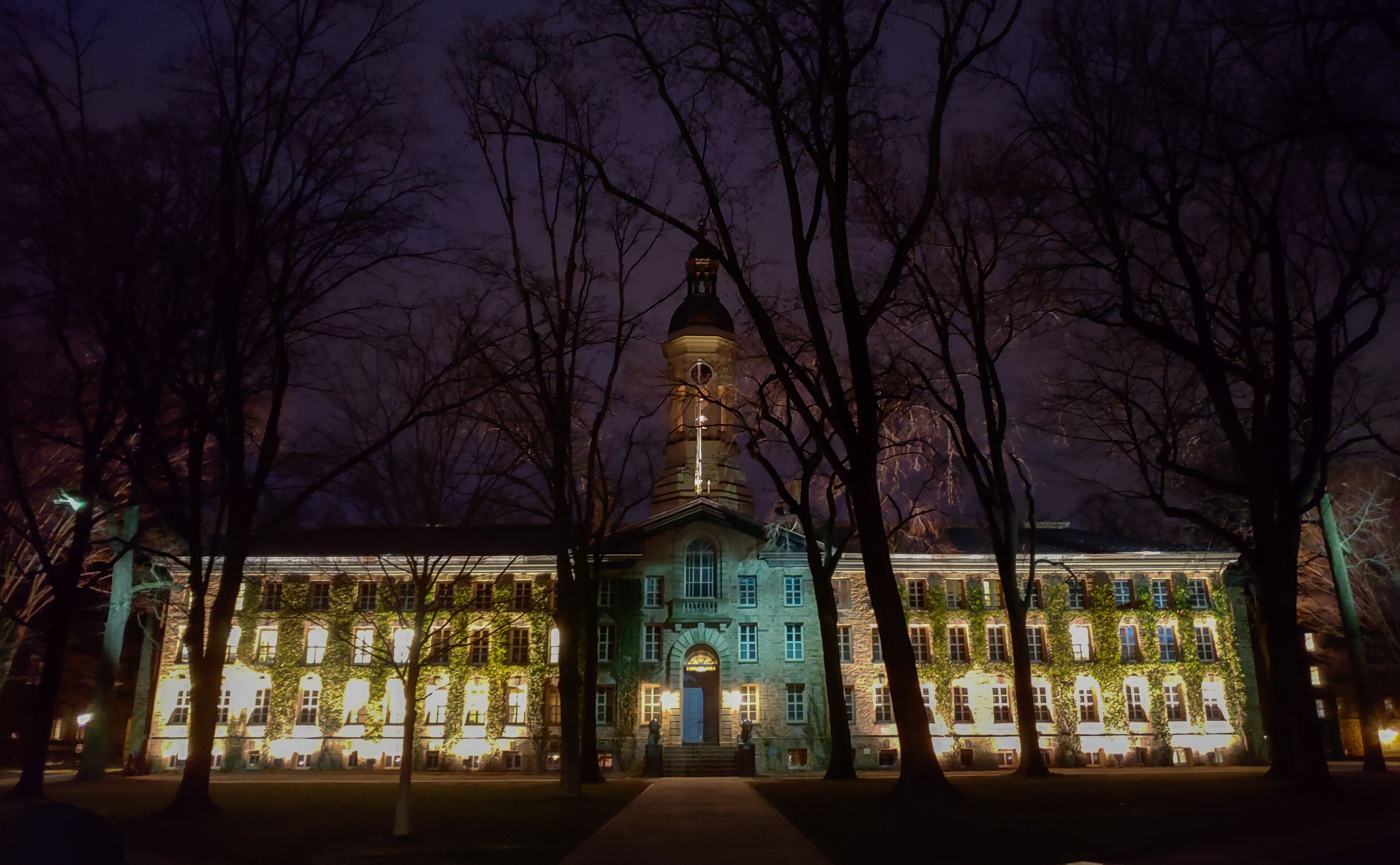 A historic building with a tower, surrounded by trees and illuminated by lights.