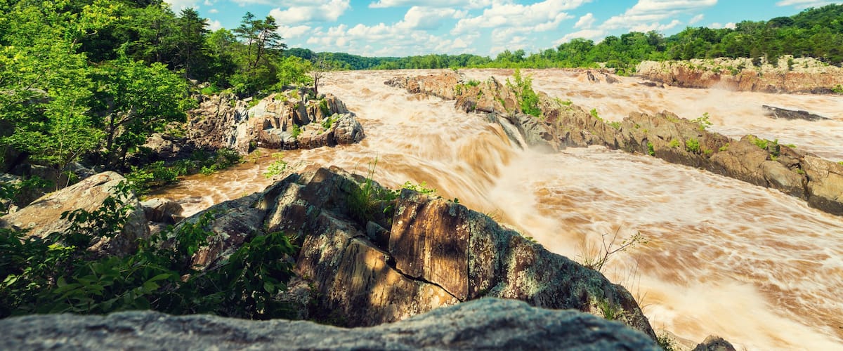 A river with a waterfall surrounded by lush greenery and a clear blue sky.