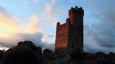 A stone tower with a steep, narrow staircase leading up to it, surrounded by rocky terrain and a cloudy sky.