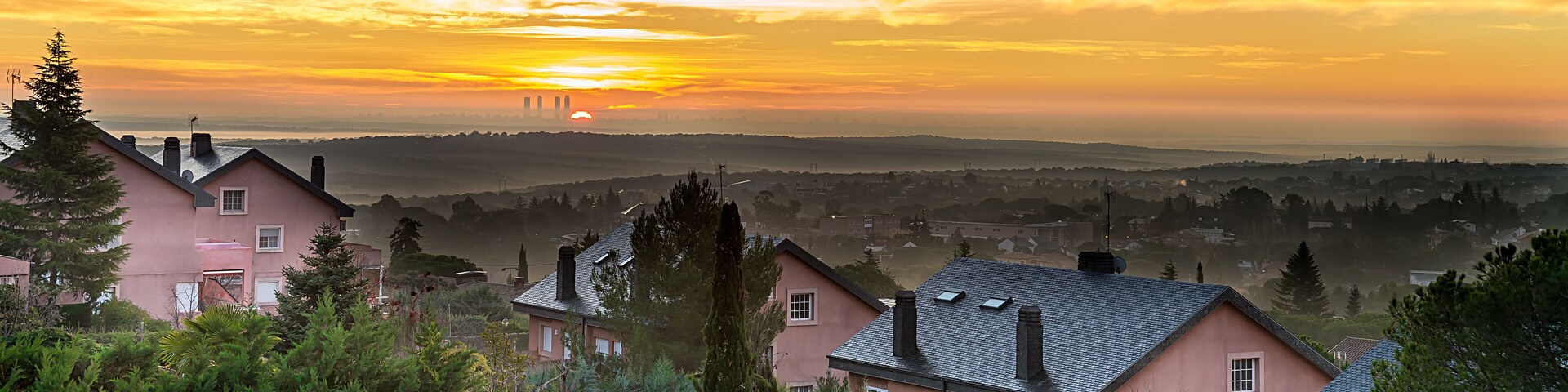 A pink house with a black roof, surrounded by greenery and a sunset in the background.