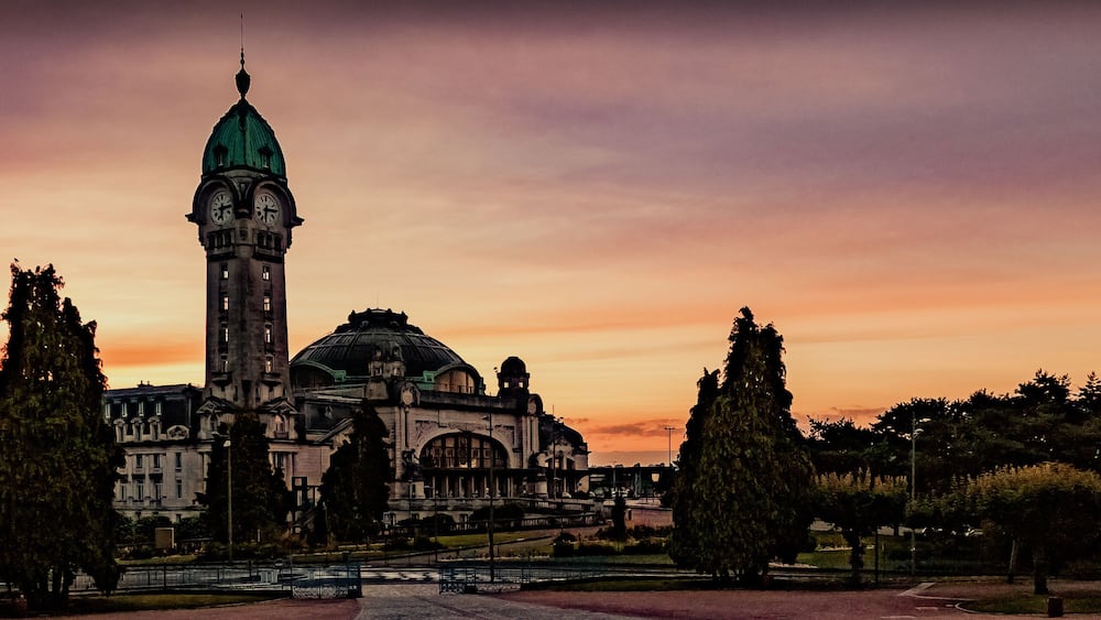 A historic building with a clock tower and dome, surrounded by trees and a sunset sky.