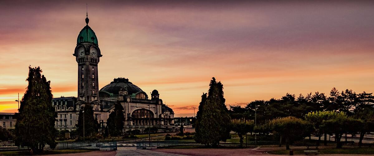 A historic building with a clock tower and dome, surrounded by trees and a sunset sky.