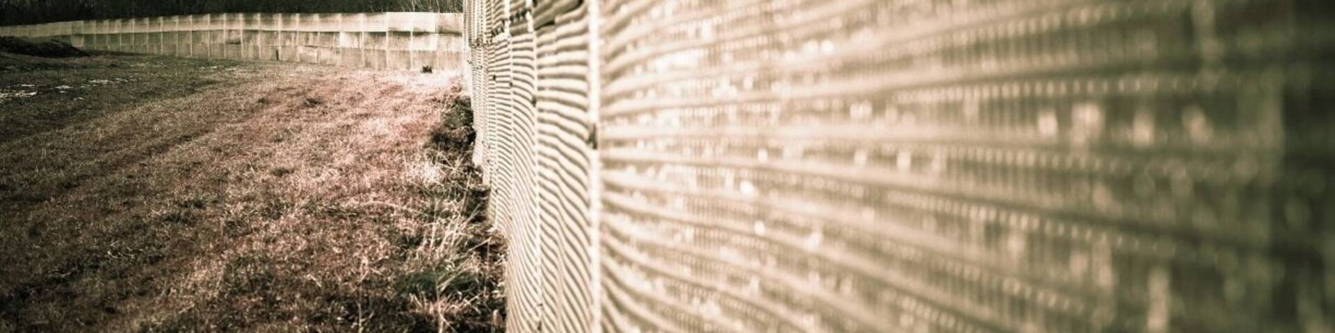 Part #7: Outer Fence
The outer fences were constructed in a number of phases, starting with the initial fortification of the border from May 1952.
This Photo is showing a "third-generation" fence, much more solidly constructed (1960s to the 1980s). The fence line was moved back to create an outer strip between the fence and the actual border. The barbed-wire fences were replaced with a barrier that was usually 3.2–4.0 metres (10–13 ft) high, like this.
The openings in the mesh were generally too small to provide finger-holds and were very sharp. The panels could not easily be pulled down, as they overlapped, and they could not be cut through with a bolt- or wire-cutter. Nor could they be tunnelled under easily, as the bottom segment of the fences was partially buried in the ground.