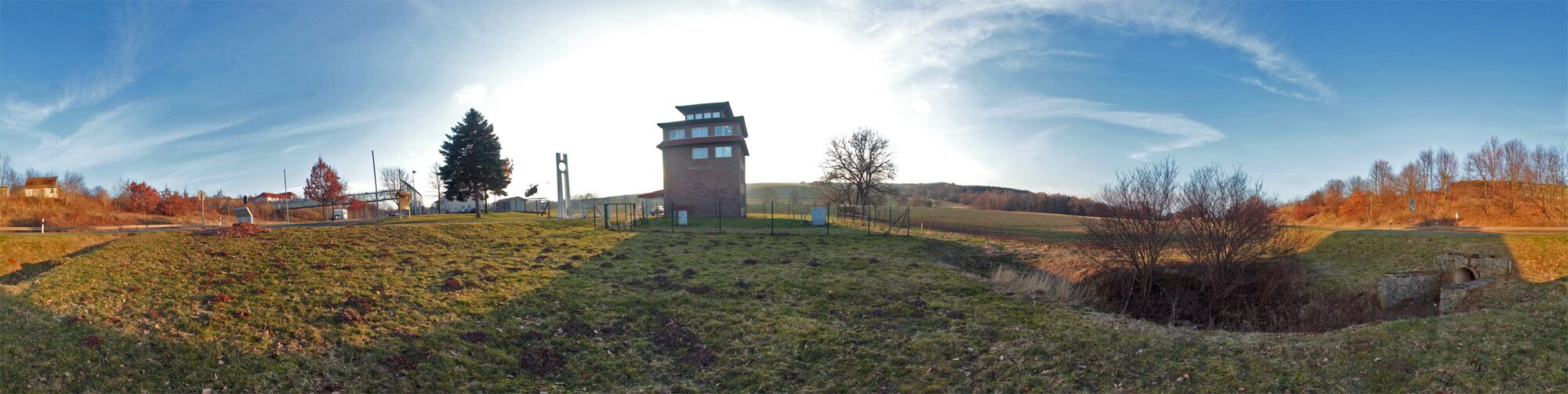 A grassy hill with a tower-like structure, a large tree, and a clear sky.
