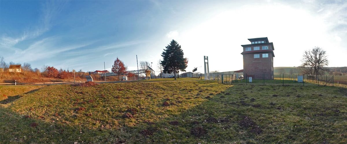 A grassy hill with a tower-like structure, a large tree, and a clear sky.