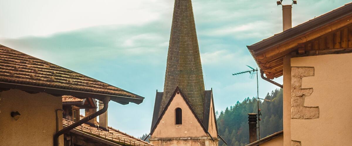 A narrow street with buildings on either side, a church with a clock tower, and a mountain in the background.