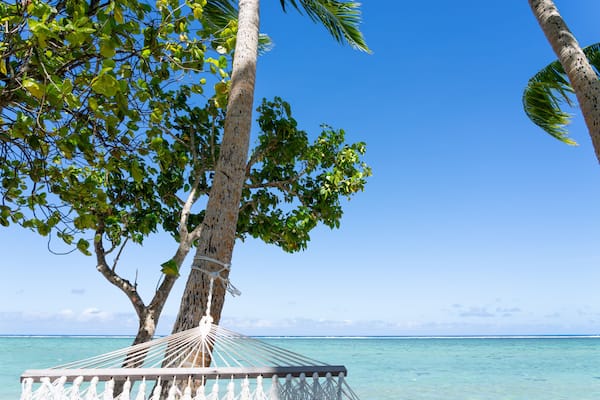 White rope hammock tied to coconut palm tree at waters edge