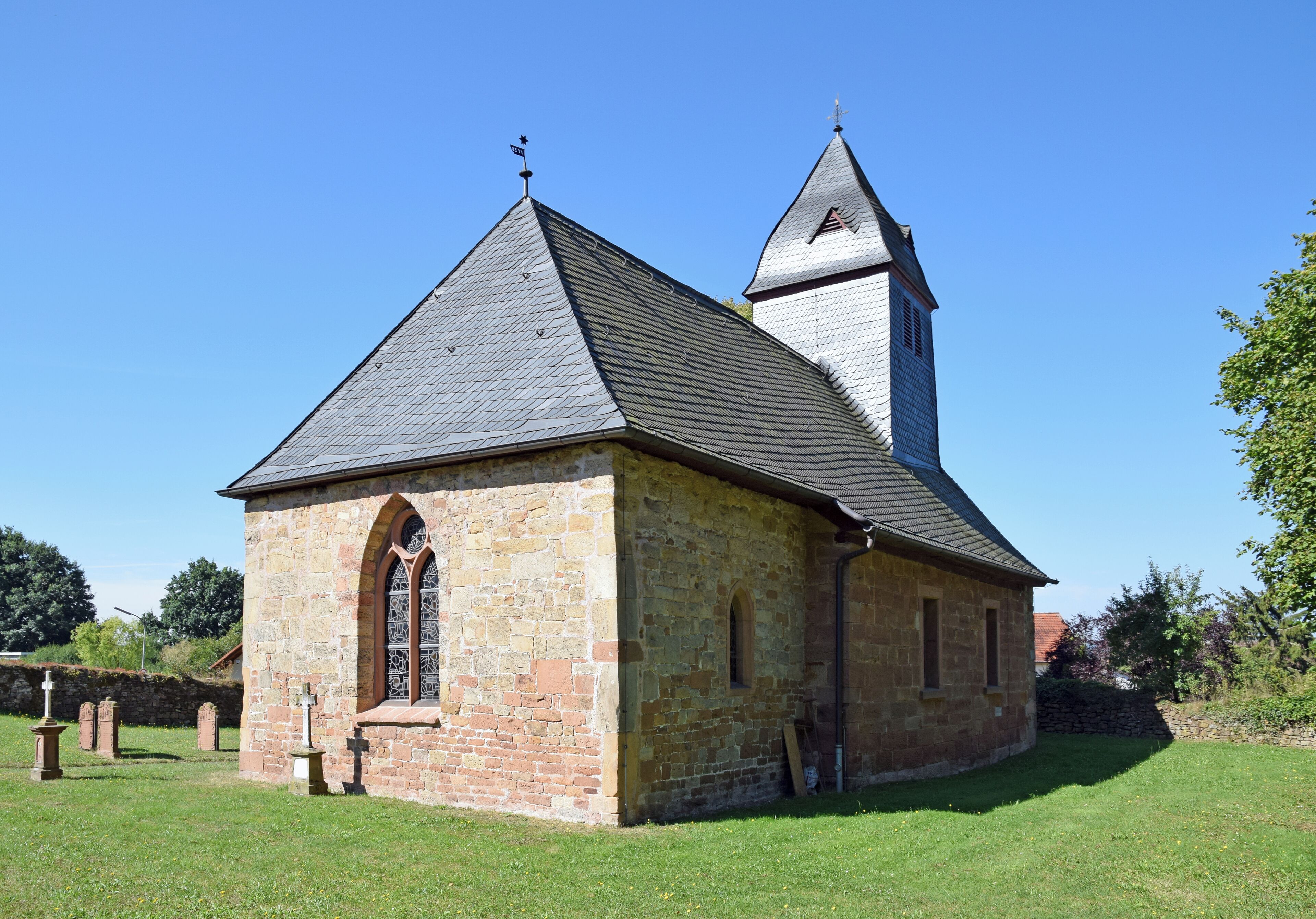A stone church with a bell tower and a grassy cemetery.