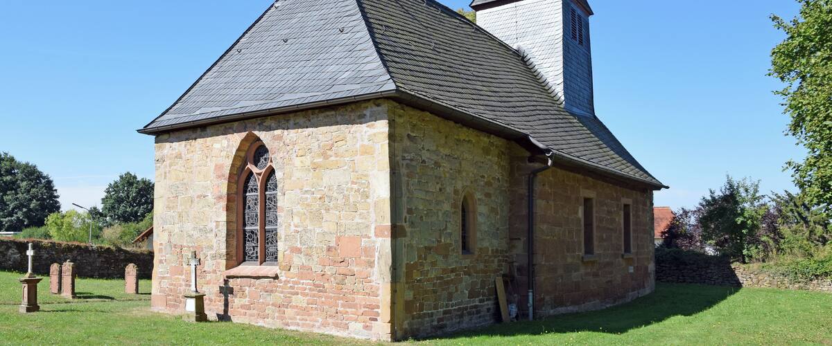 A stone church with a bell tower and a grassy cemetery.
