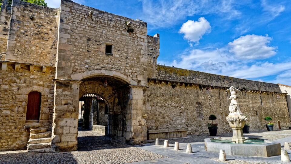 A historic stone building with an arched entrance, a courtyard with a fountain, and cobblestone pavement.