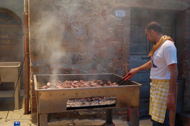 A person grilling meat outdoors with a brick wall and a number 16 sign in the background.