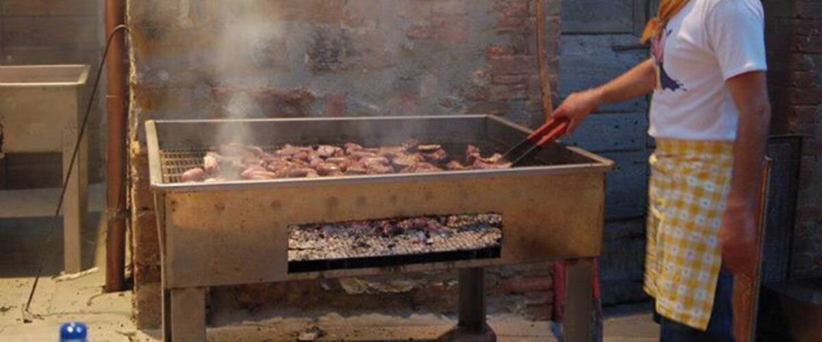 A person grilling meat outdoors with a brick wall and a number 16 sign in the background.