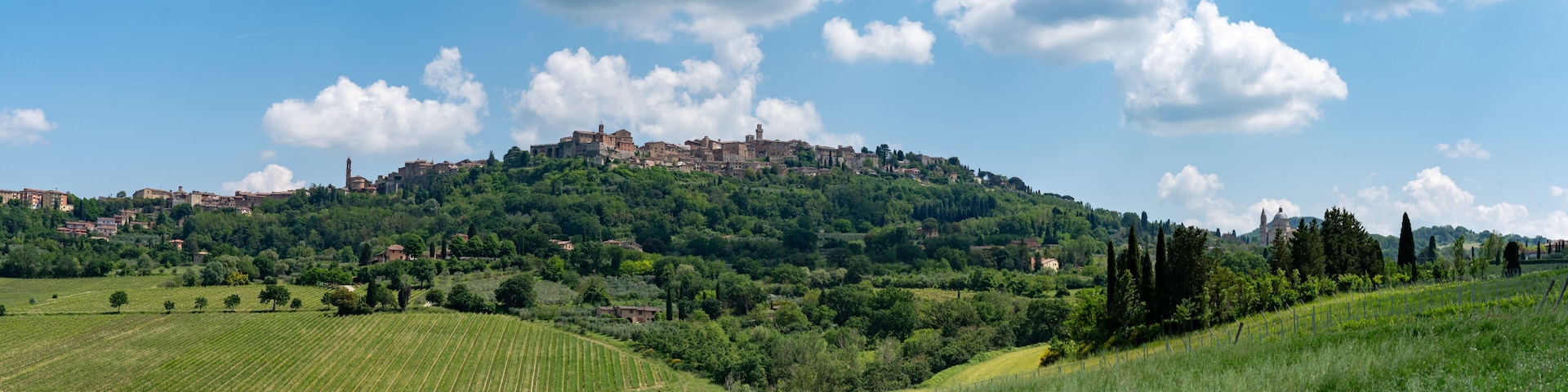 A hilltop town with historic buildings, lush green fields, and a clear blue sky.