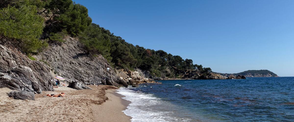 A coastal beach with rocky cliffs, a clear blue sky, and calm sea waves.
