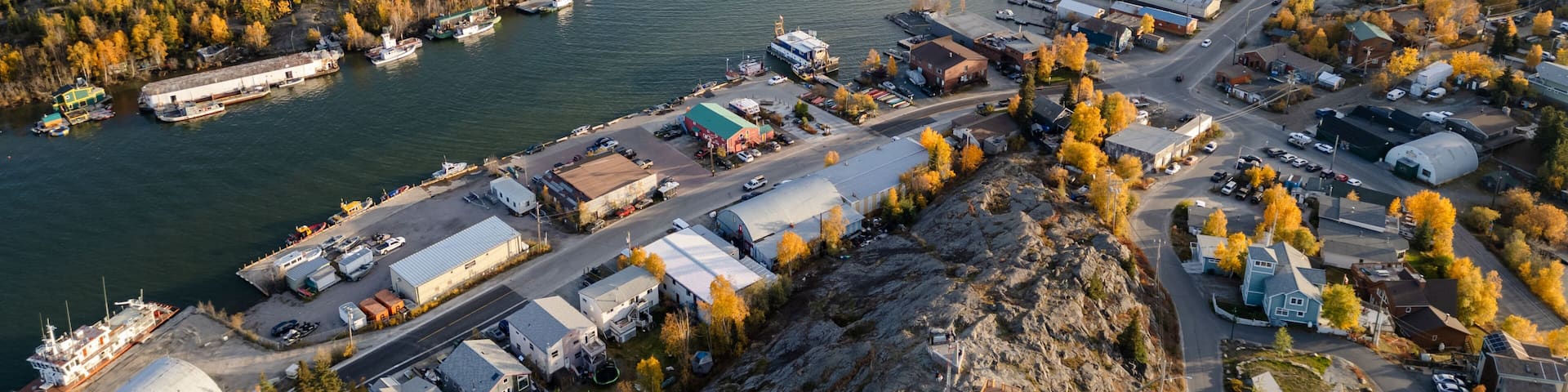 A coastal town with a marina, autumn foliage, and industrial buildings.
