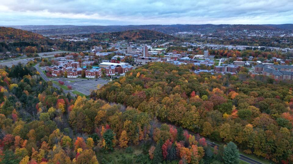 arial view of binghamton university in vestal, new york during autumn with fall foliage (leaves changing colors) at dusk, sunset, cloudy sky (library tower, student union, mountainview residence hall)