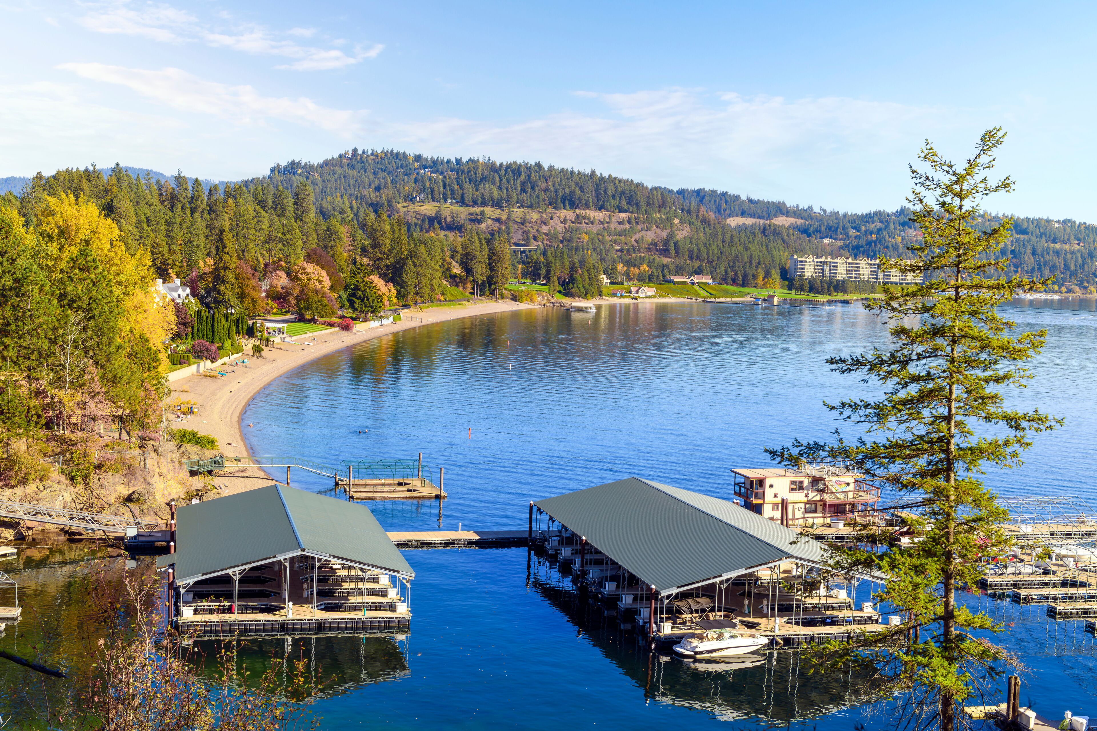 A lake with a dock, a boat, and a building with a green roof.