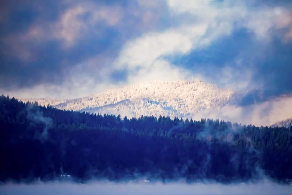 Lumipeitteinen vuoristo, jonka edessä on metsä ja jonka takana avautuu sumuinen laakso.