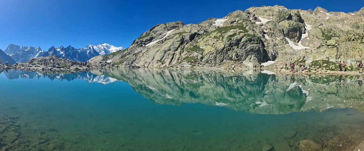 A mountain lake with clear reflections, rocky terrain, and snow-capped peaks.