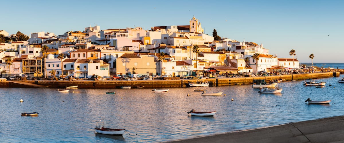 A coastal town with white buildings, a prominent church, and numerous boats on the water.