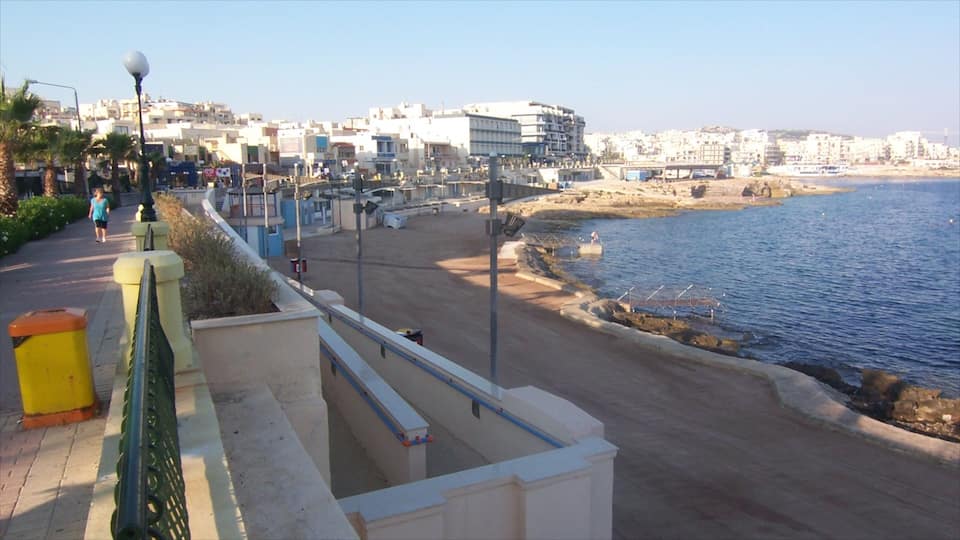 Une promenade en bord de mer offrant une vue dégagée sur l’océan, un sentier piétonnier et des bâtiments en arrière-plan.