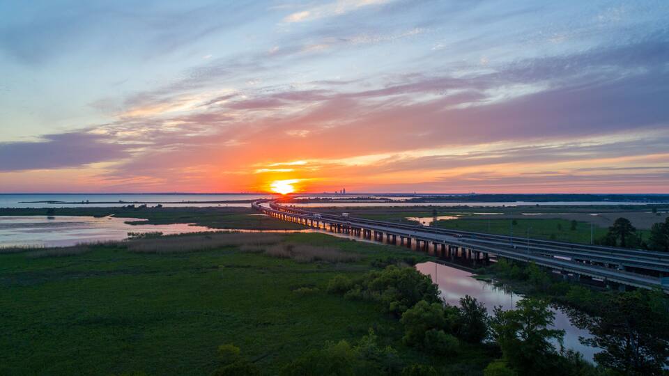 A sunset over a coastal landscape with a bridge extending into the distance.