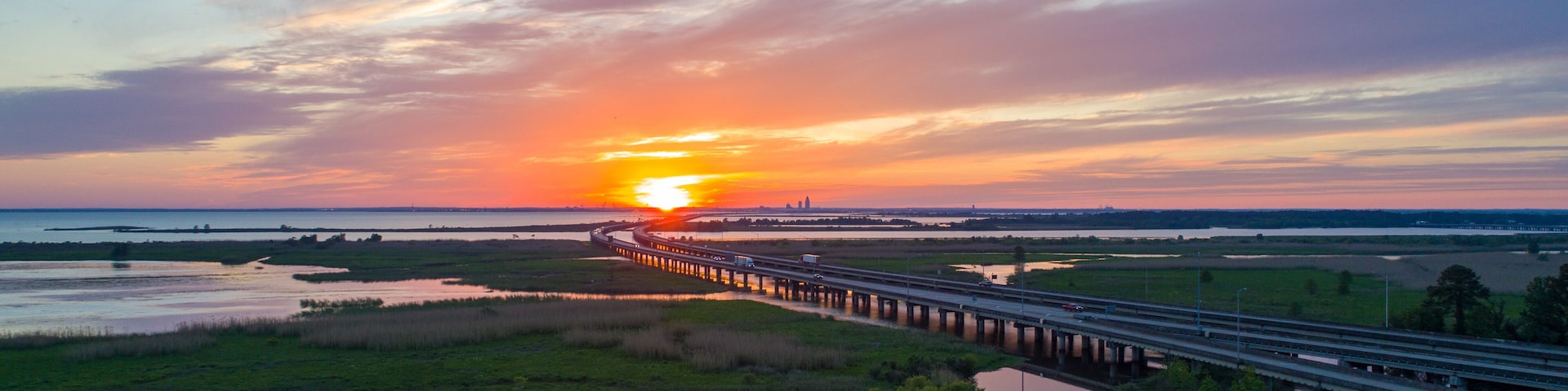 A sunset over a coastal landscape with a bridge extending into the distance.