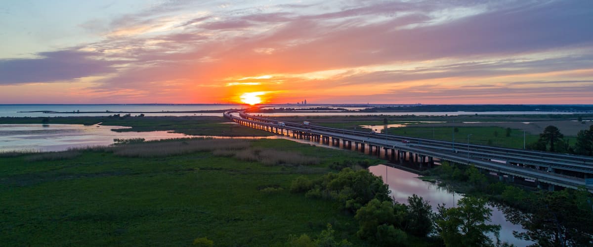 A sunset over a coastal landscape with a bridge extending into the distance.