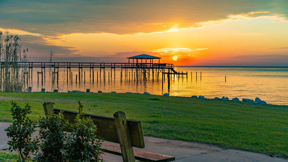 A sunset over a calm lake with a wooden pier and a bench in the foreground.
