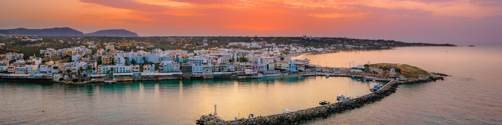 Un pueblo costero con edificios coloridos, un mar tranquilo y un cielo al atardecer.