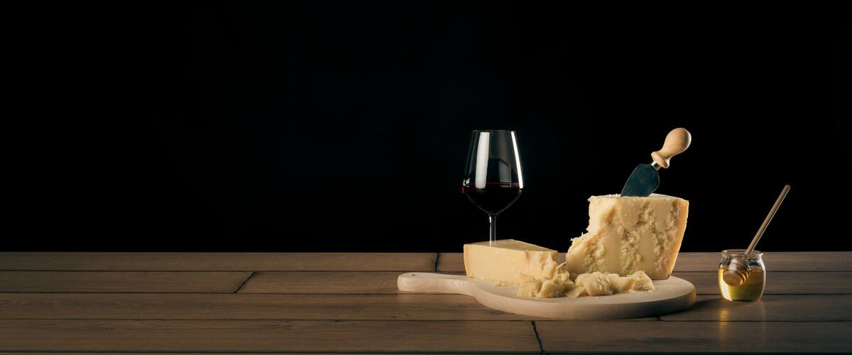 A wooden table with a piece of cheese, a glass of red wine, and a honey dipper.