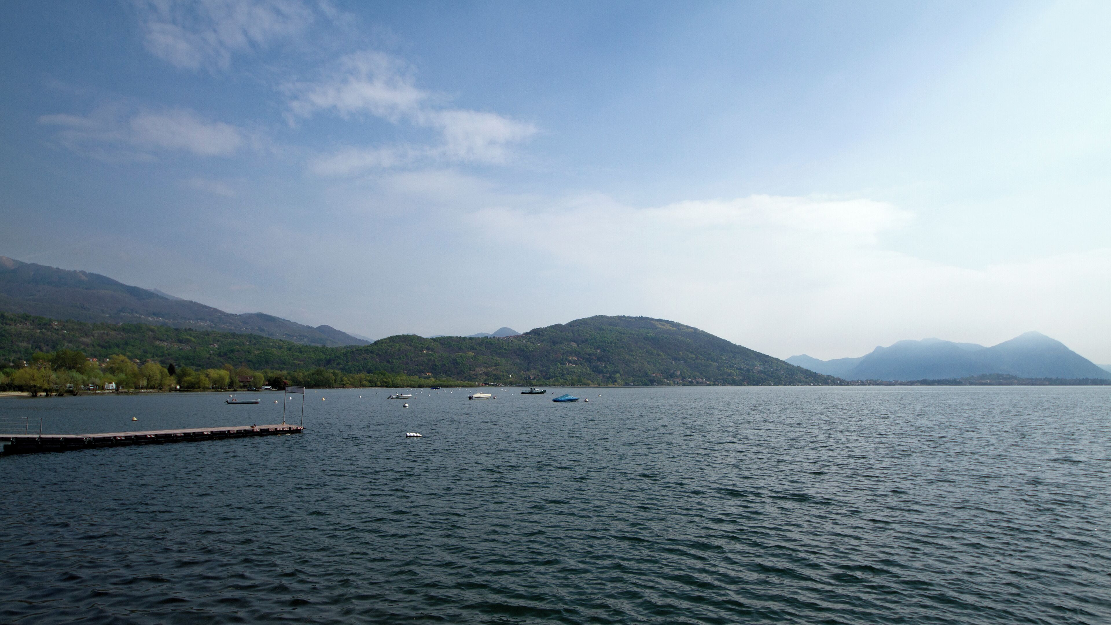 A calm lake with boats, a dock, and mountains in the background.