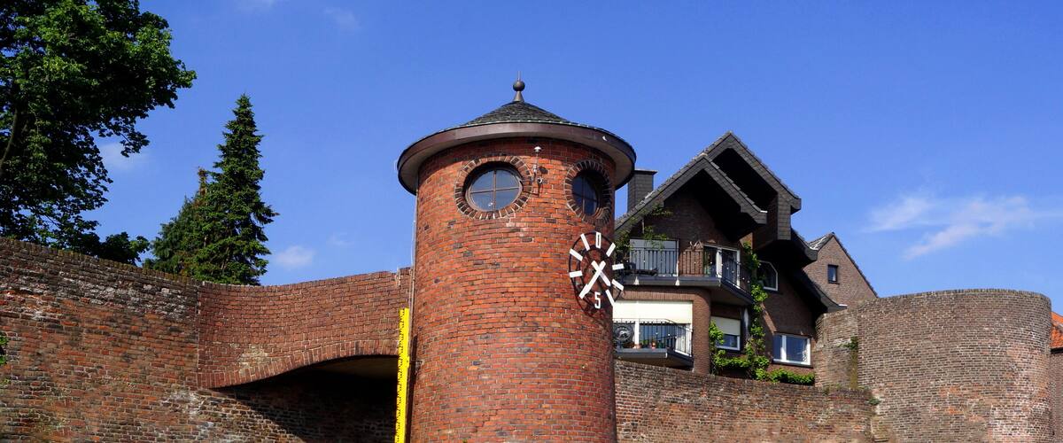 A historic brick tower with a clock, a modern house with a sloped roof, and a clear blue sky.