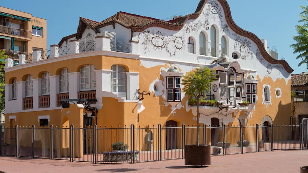 Un bâtiment aux murs jaunes et blancs, orné de décorations élaborées et surmonté d’un toit recouvert de tuiles.