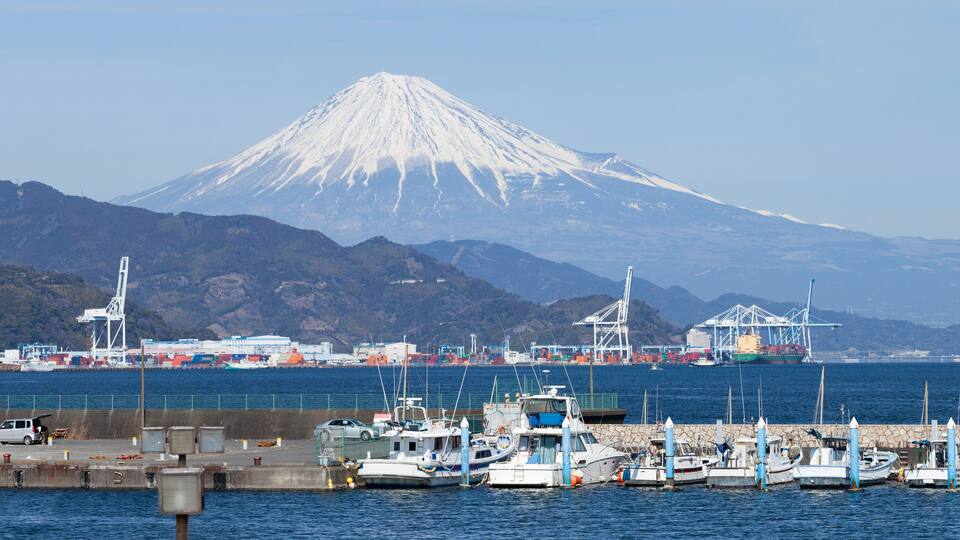 A harbor with boats, a port with cranes, and a snow-capped mountain in the background.
