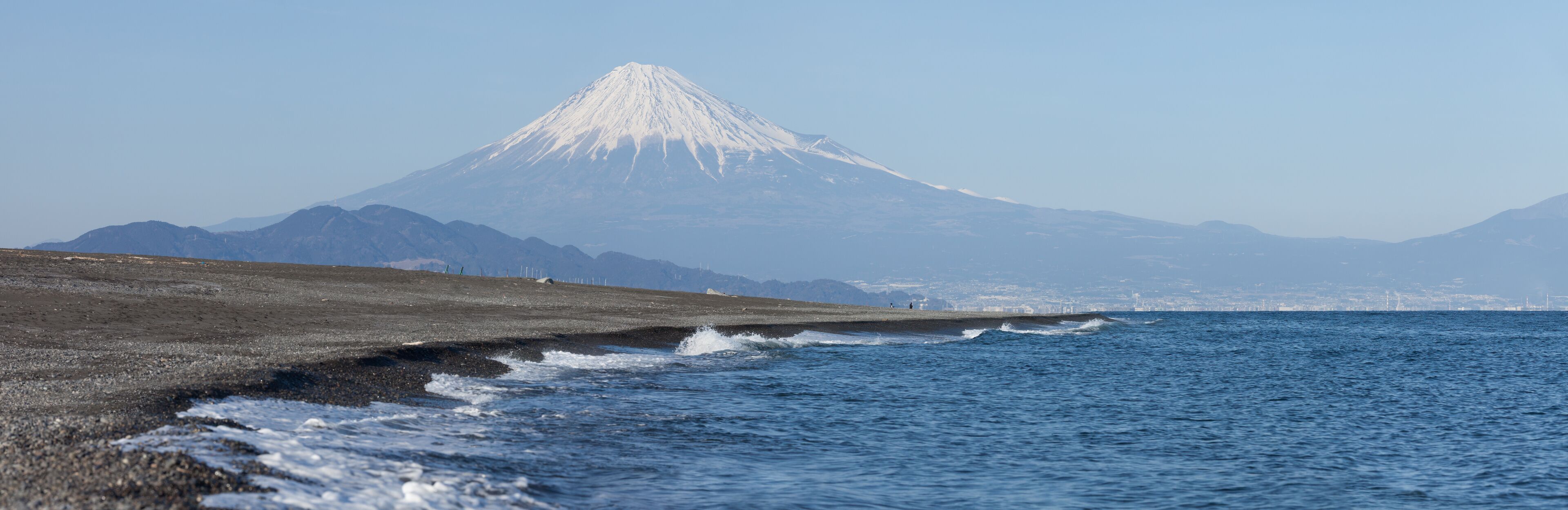 A coastal landscape with a snow-capped mountain in the background.