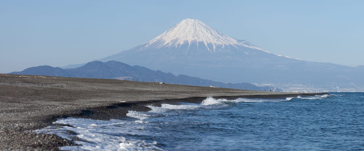 A coastal landscape with a snow-capped mountain in the background.