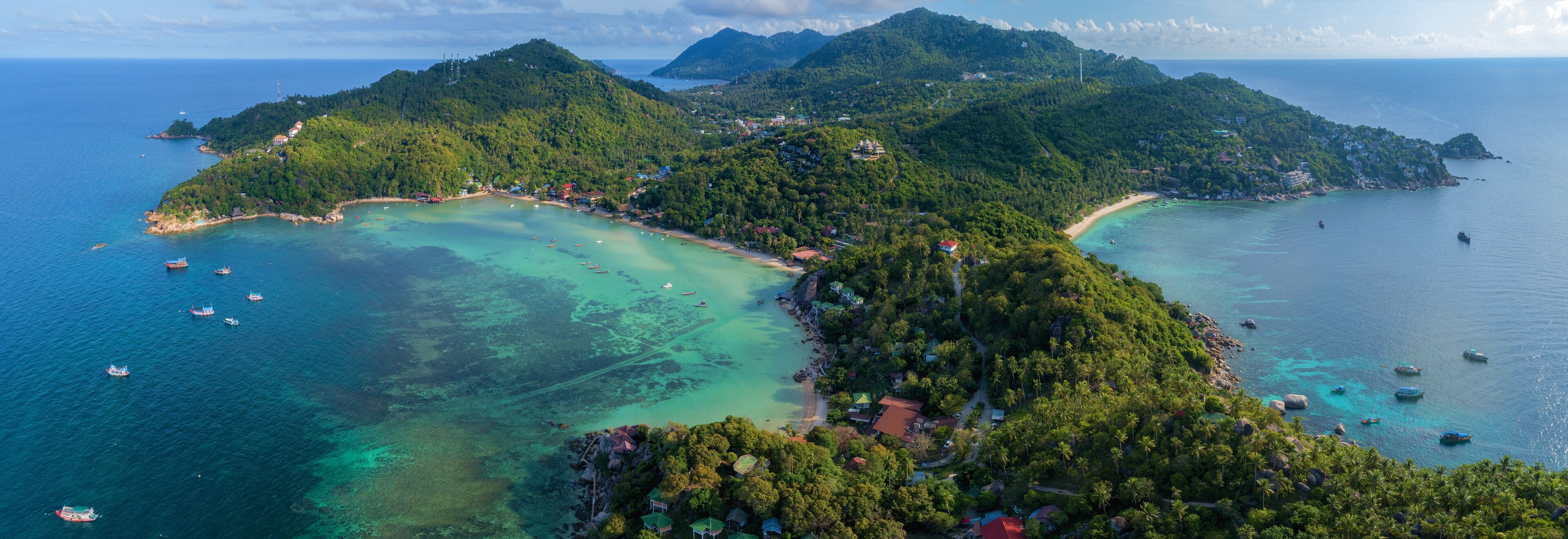 A tropical island with clear turquoise waters, surrounded by lush green hills and scattered houses.