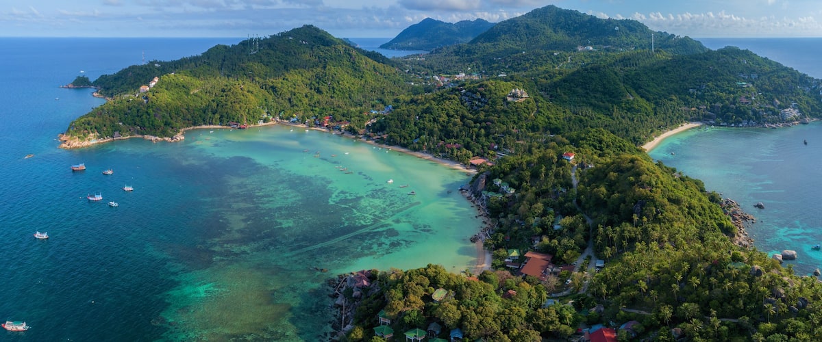 A tropical island with clear turquoise waters, surrounded by lush green hills and scattered houses.
