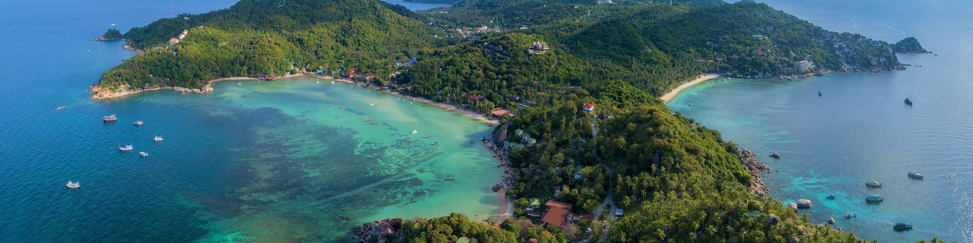 A tropical island with clear turquoise waters, surrounded by lush green hills and scattered houses.