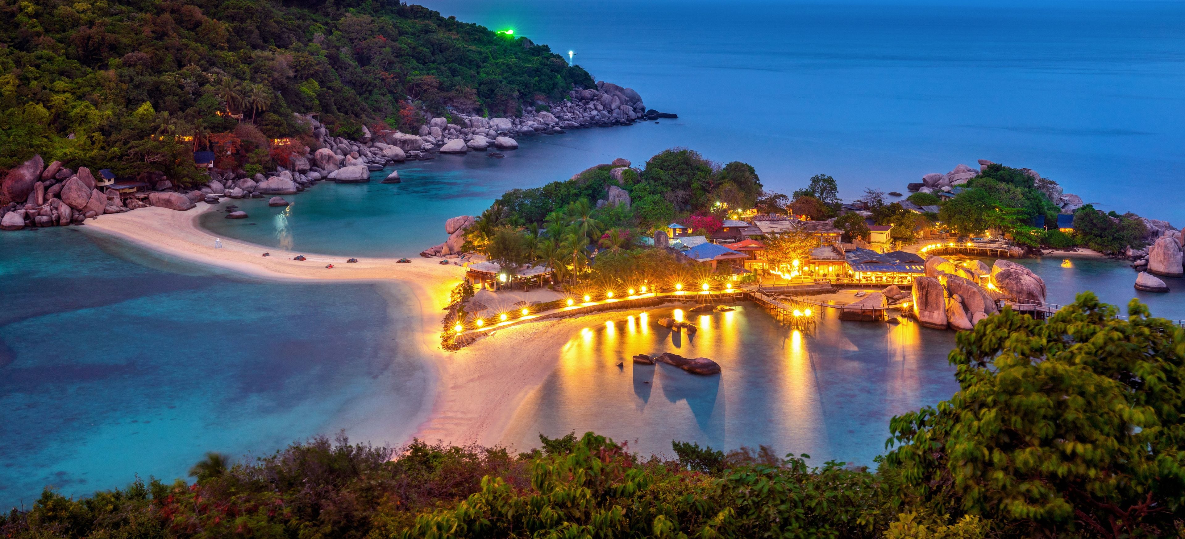 Un complejo turístico frente al mar, con playa, aguas cristalinas y estructuras iluminadas.