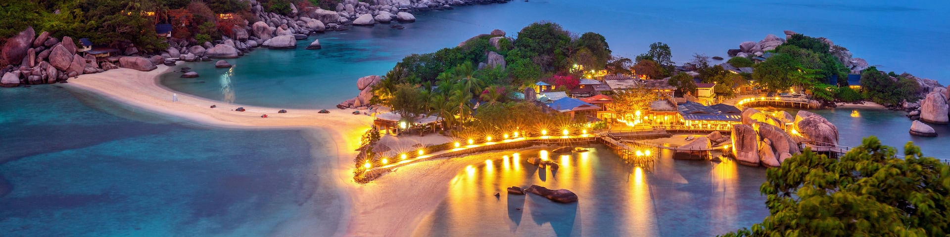 Un complejo turístico frente al mar, con playa, aguas cristalinas y estructuras iluminadas.