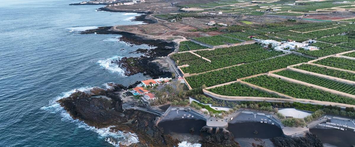 A coastal landscape with rocky cliffs, a beach, and agricultural fields.