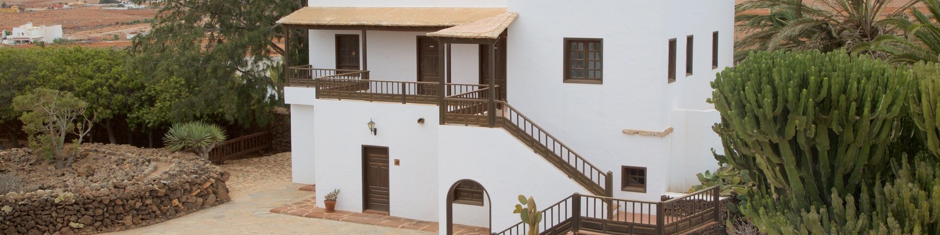 A white two-story house with a balcony, surrounded by cacti and desert vegetation.