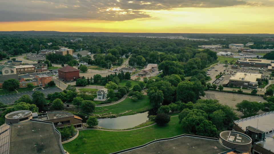 A town with a church, a large brick building, and a lake surrounded by greenery.