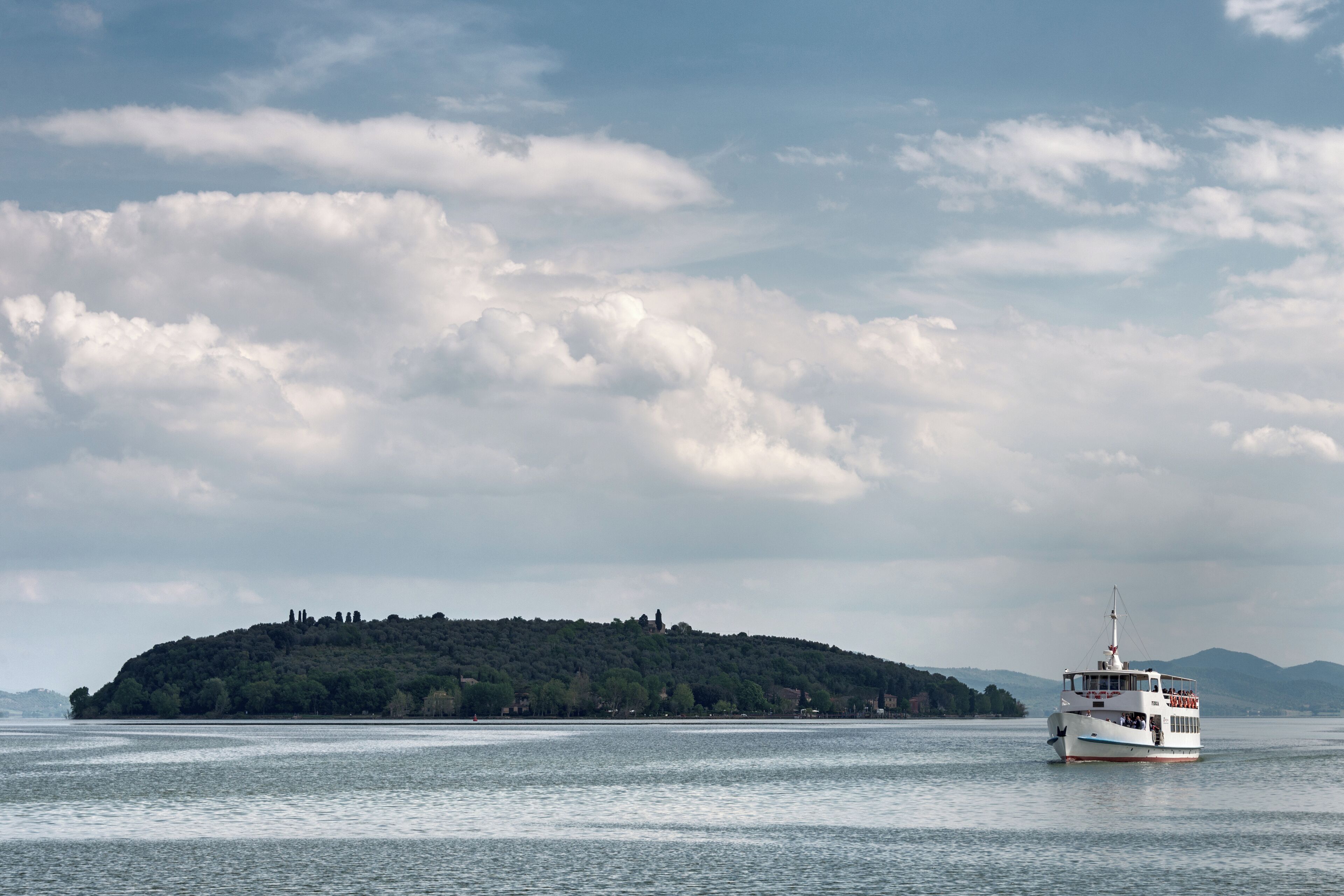 A boat on a calm body of water with a forested island in the background.