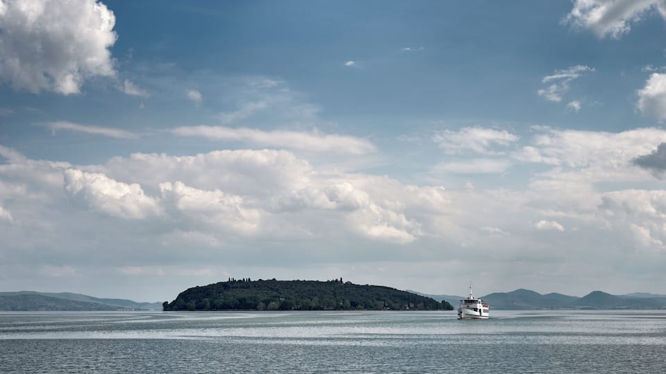 A white boat on a calm body of water with a forested island in the distance and mountains in the background.
